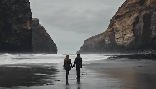 Пара идет рука об руку по тихому черному пляжу с высокими обветренными скалами позади.