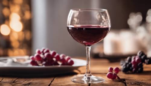 A crystal wine glass half-filled with rich burgundy wine, situated on a rustic wooden table.