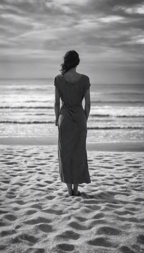 Une image en noir et blanc d&#39;une femme debout seule sur une plage déserte.