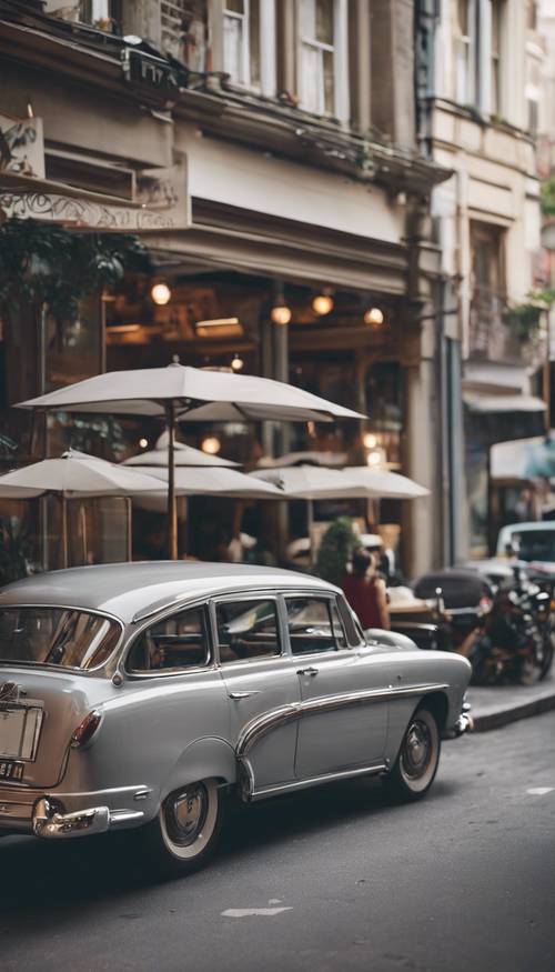 Ein hellgrauer Oldtimer, der neben einem belebten, angesagten Café in einer geschäftigen Stadt geparkt ist.