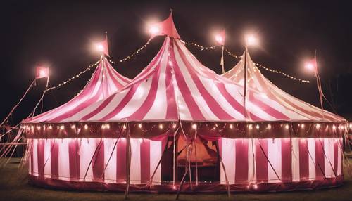 A circus tent with pink and white stripes illuminated with festive lights.