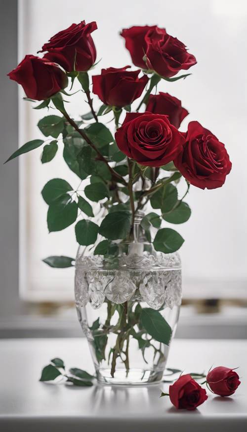 Un ramo de rosas rojas adornado pero simplista dispuesto en un jarrón de vidrio transparente sobre una mesa blanca.