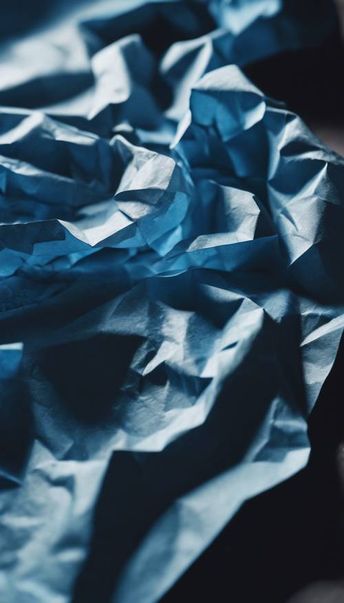 A closeup view of blue paper crumpled with a light shining on it, casting a dramatic shadow.