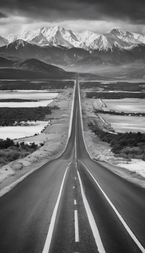 一幅黑白全景照片，描绘了一条笔直的长公路通往白雪皑皑的山脉。