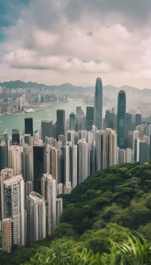 Aerial view of Hong Kong skyline with skyscrapers and the iconic Victoria Peak surrounded by lush greenery in the background.
