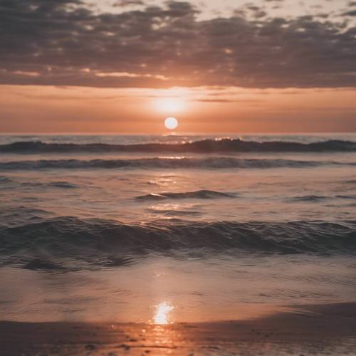 Wyluzowana scena na plaży z zachodem słońca w kolorze różowego złota odbitym w spokojnych falach oceanu.