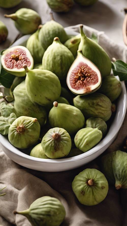 A white porcelain bowl filled with ripe green figs set on a naturally lit kitchen table.
