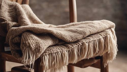 An earth-toned woolen blanket neatly folded on a vintage wooden chair with a backdrop of a plastered wall. Tapet [33bf98a44507498abdfe]