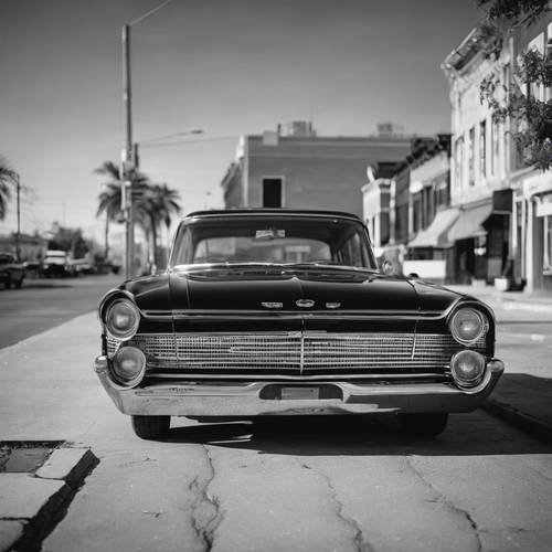Ein Foto eines klassischen amerikanischen Autos aus den 1960er Jahren, das in einer verlassenen Straße geparkt ist, präsentiert in Schwarzweiß.