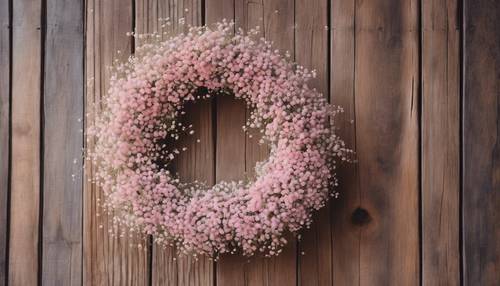 Une couronne composée de fleurs de gypsophile rose pastel accrochées à une porte rustique en bois.