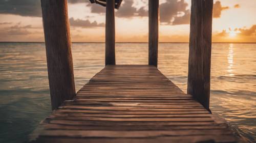 Um cais rústico de madeira que se estende pelas águas calmas da praia de Miami, com um pôr do sol profundo ao fundo.