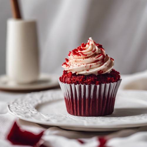 A red velvet cupcake with a twirl of cream cheese frosting on a white linen tablecloth.