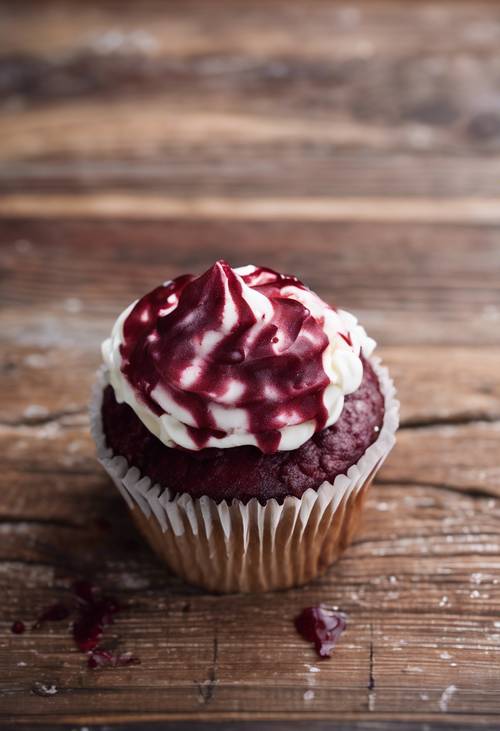 An overhead view of a maroon-colored velvet cupcake adorned with creamy white frosting on a distressed wooden table.
