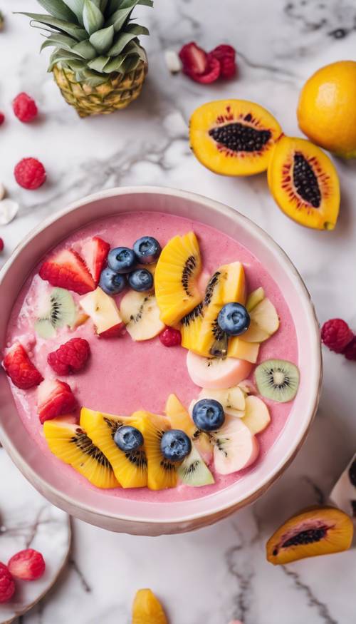 A pastel pink smoothie bowl adorned with perfectly arranged, colourful slices of exotic fruits, on a white marble countertop.