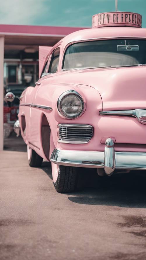 A retro car painted in pastel pink parked in a 1950s style gas station.
