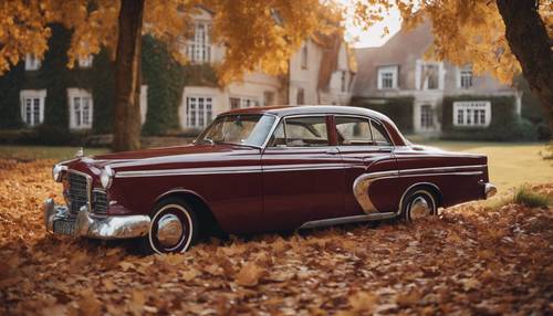A maroon classic vintage car parked near a countryside house with fallen leaves around.
