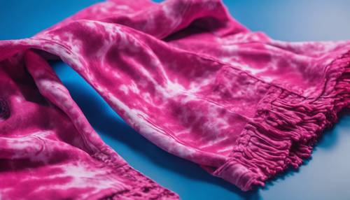 Un pañuelo teñido anudado de color rosa brillante doblado cuidadosamente sobre un fondo azul.