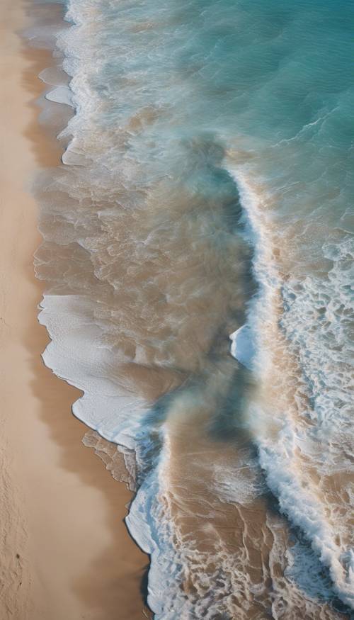 An aerial view of the brilliant baby blue ocean washing up against a sandy shore.