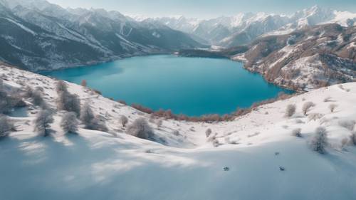 Una vista aérea de un tranquilo lago de color azul claro rodeado de montañas cubiertas de nieve.