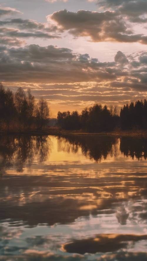 Spokojne jezioro o zachodzie słońca ze złotymi odcieniami odbijającymi się w spokojnej wodzie.