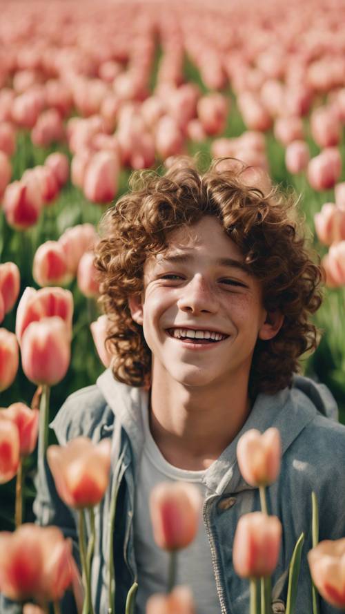 Uma imagem em close de um adolescente com cabelos castanhos cacheados e sardas, rindo muito em um campo de tulipas sob o sol do meio-dia.