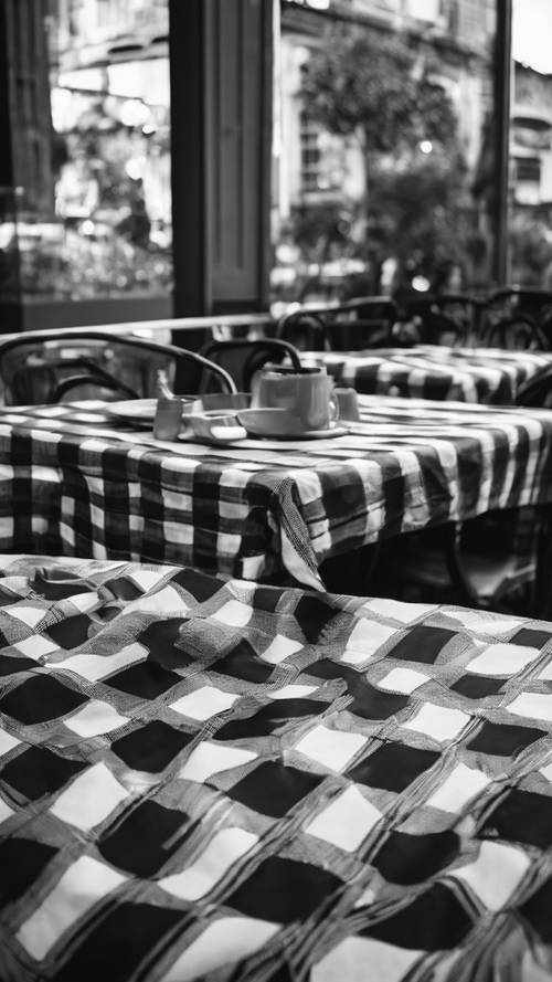 Kawiarniane patio z obrusem w czarno-białą kratę rozłożonym na stołach.