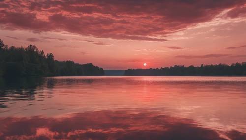Matahari terbenam berwarna merah pastel di atas danau yang tenang.
