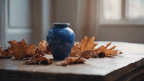 A still life composition featuring a round, blue porcelain vase filled with dried, brown autumn foliage.