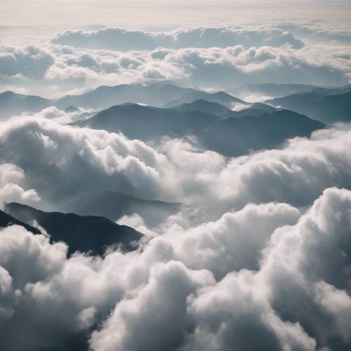 Topos de montanhas aparecendo através de um manto de nuvens brancas e espessas.