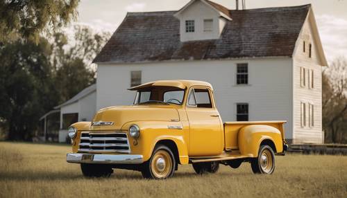 An antique yellow Chevy pickup truck parked in front of a historic farmhouse.