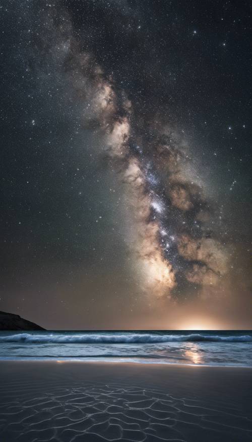 Una playa de arena negra bajo un cielo nocturno cristalino y estrellado que muestra la Vía Láctea.