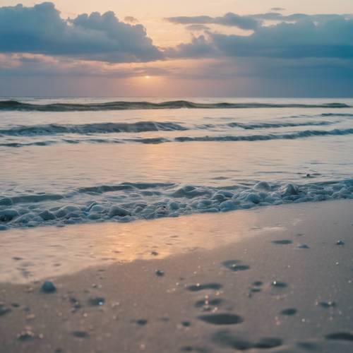 A peaceful beach scene at dawn, the soft blue sea merging with the sky at the horizon.