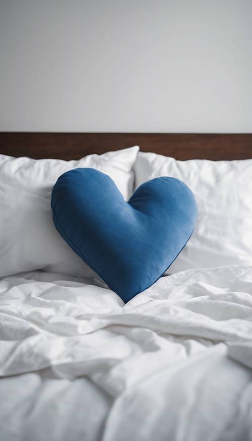 Ein blaues herzförmiges Kissen auf einem weißen minimalistischen Bett.