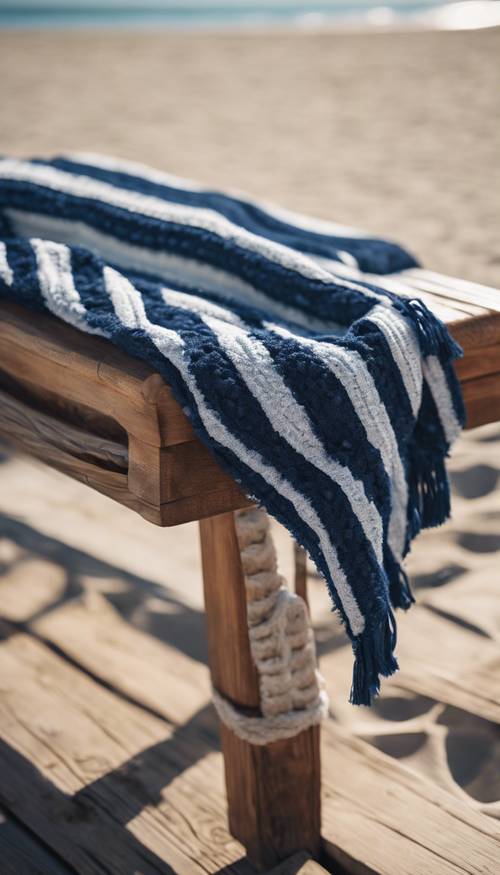 明亮的海滩环境中，一条经典的海军条纹毯子精美地铺在木凳上。
