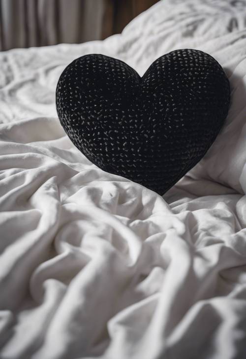 A black velvet heart-shaped pillow sitting comfortably on a pristine white bedspread. Tapet [cb0f5627774c481c8854]