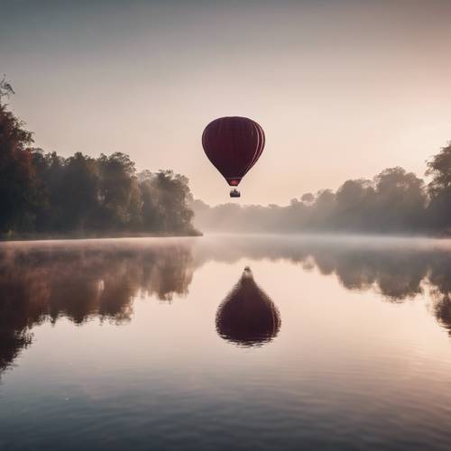A maroon hot air balloon hovering over a serene lake during the early morning mist.